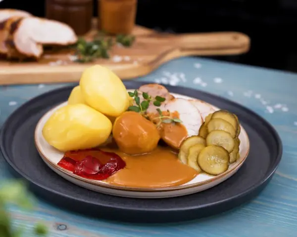 En tallrik med skivad ytterfile i sockerkaksform, potatis, sås, gelé och gurka.