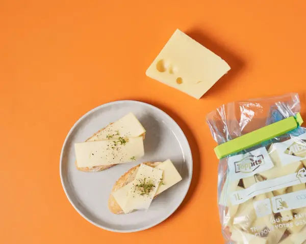 Slices of cheese on bread on a plate, a wedge of cheese, and a bag of cheese chunks.