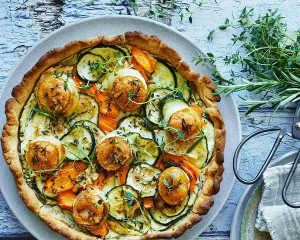 En gyllene, smakrik vegetarisk paj fylld med zucchini, morötter och toppad med ost. Garnerad med färska örter.
