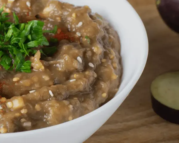 En krämig baba ganoush, toppad med färsk persilja och paprikapulver, bredvid skivade auberginer.
