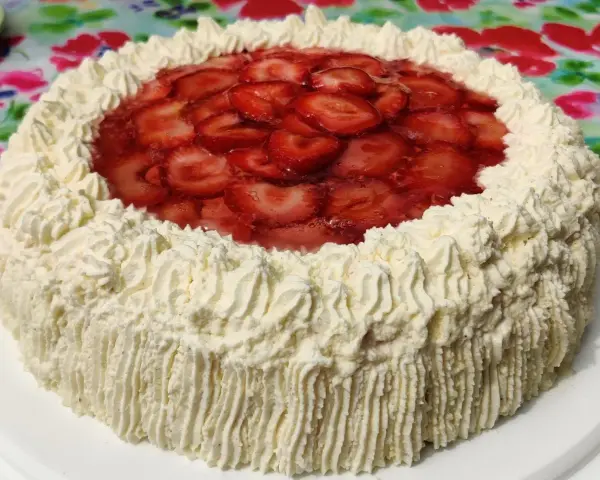 A round cake with whipped cream frosting and sliced strawberries on top.
