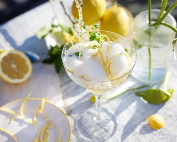 En bubblig drink med citronskal och mynta hälls upp i ett glas. Perfekt att bjuda på fika till många.