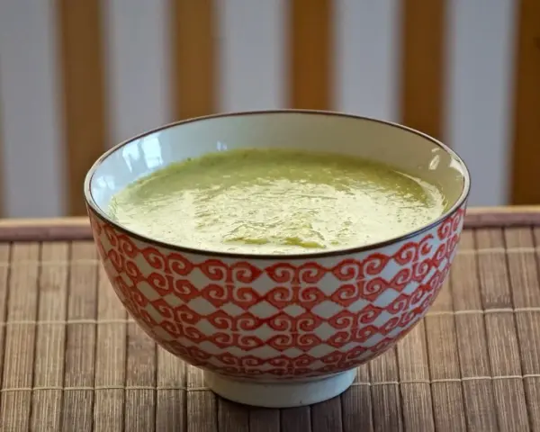 En skål med krämig blomkål och broccolisoppa, serverad på en bambumatta.