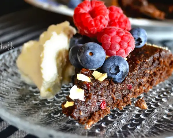 En bit nyttig kladdkaka med bär och grädde på ett mönstrat fat.