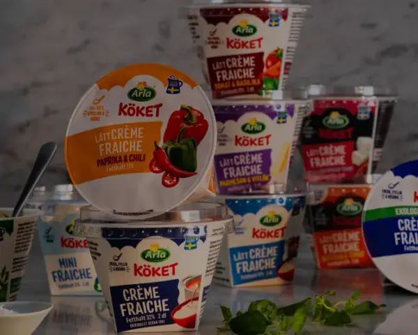Various Arla Köket crème fraîche tubs, some open, with herbs and a bowl of salt.