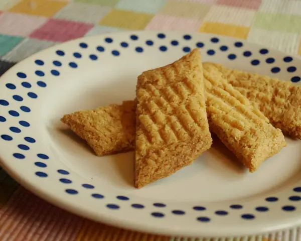 Tre gyllene glutenfria kolakakor ligger på en vit tallrik med blå prickar. De har ett rutmönster på ovansidan.