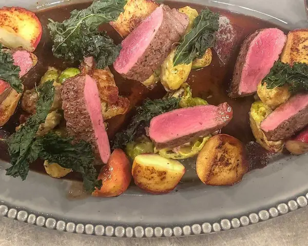 Vildsvinskött med perfekt rosa temperatur, serverat med rostade potatisar, brysselkål och grönkål i en mustig sås.