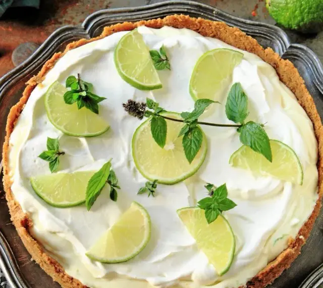 En krämig key lime pie med limeklyftor och mynta på en krispig botten, serverad på ett vackert fat.