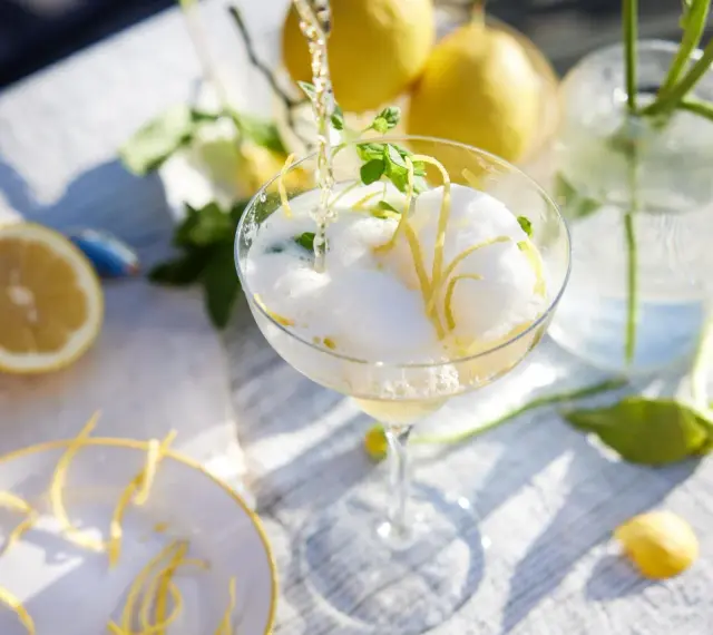 En bubblig drink med citronskal och mynta hälls upp i ett glas. Perfekt att bjuda på fika till många.