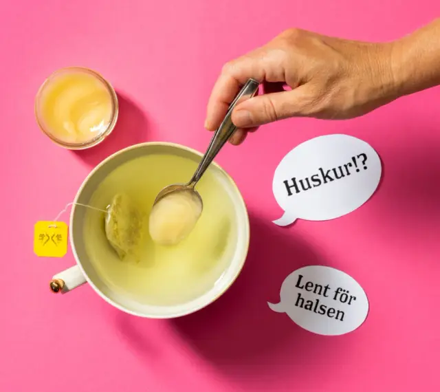 En hand lägger honung i en kopp te. Honung nyttigt för halsen, viskar pratbubblorna.