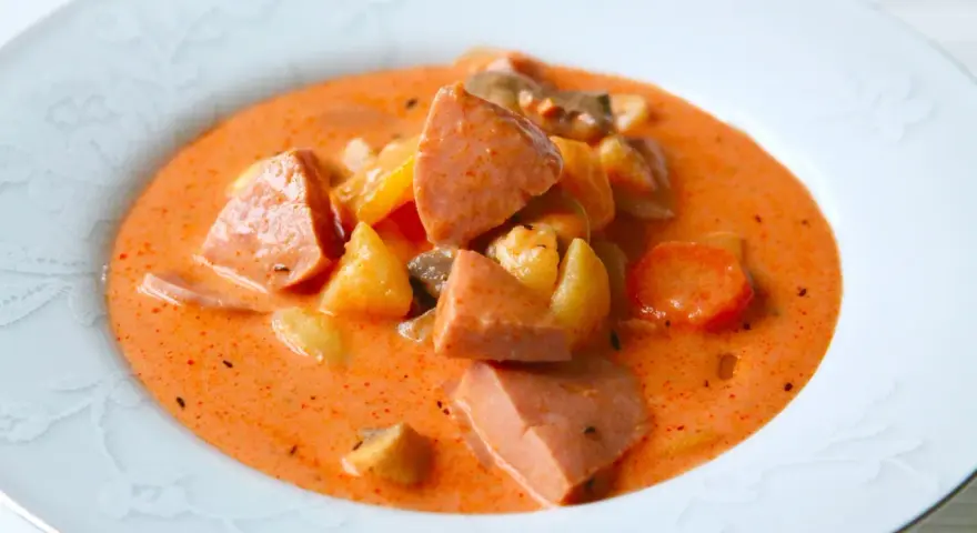 A hearty bowl of korvsoppa with sausage, potatoes, and carrots in a creamy orange broth.