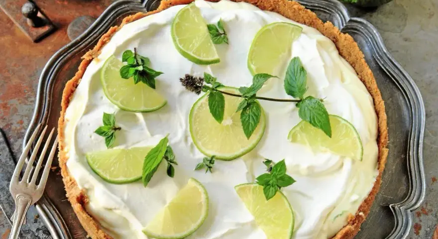 En krämig key lime pie med limeklyftor och mynta på en krispig botten, serverad på ett vackert fat.