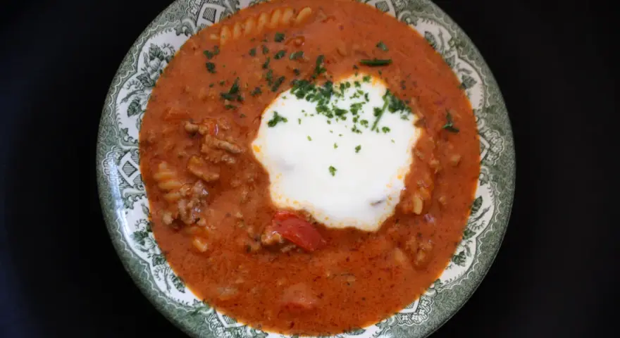 En skål med köttfärssoppa med pasta, toppad med en klick gräddfil och persilja. Perfekt köttfärssoppa med pasta för barn.