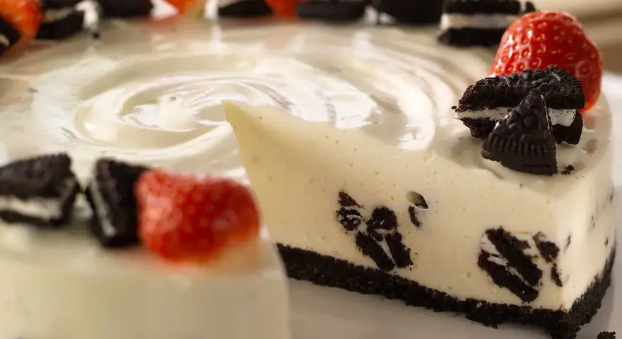 En krämig oreo cheesecake med färska jordgubbar och oreokex som dekoration. En bit är uppskuren.