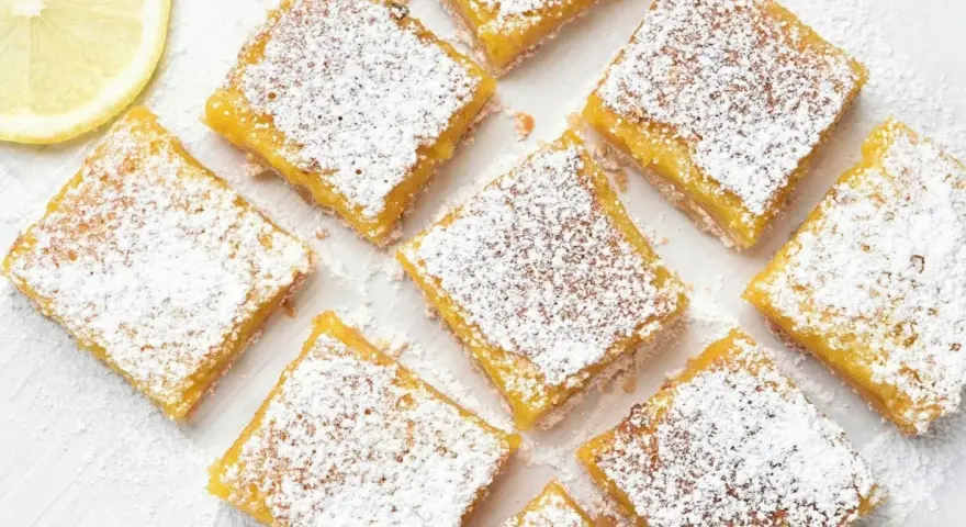 Citronkaka i långpanna, pudrad med florsocker, skuren i fyrkanter. En citronskiva syns i övre vänstra hörnet.