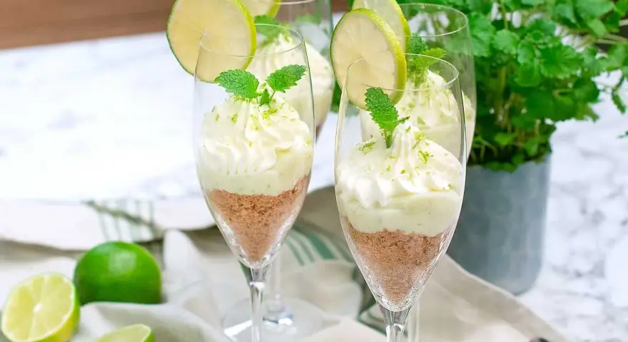 Key lime pie in glasses with whipped cream, lime slices, and mint.