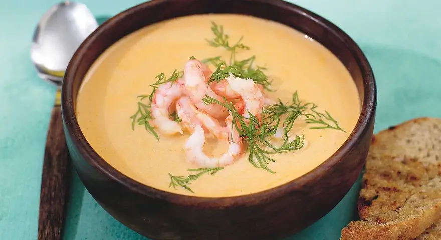 En krämig soppa med räkor och dill, serverad i en träskål med rostat bröd. En härlig soppa med räkor som värmer.