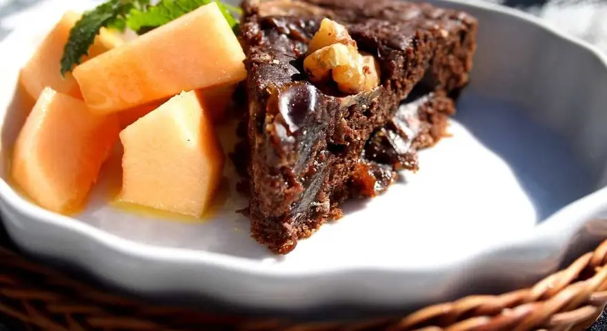 En bit saftig banankaka med choklad och nötter, serverad med färsk melon och mynta.