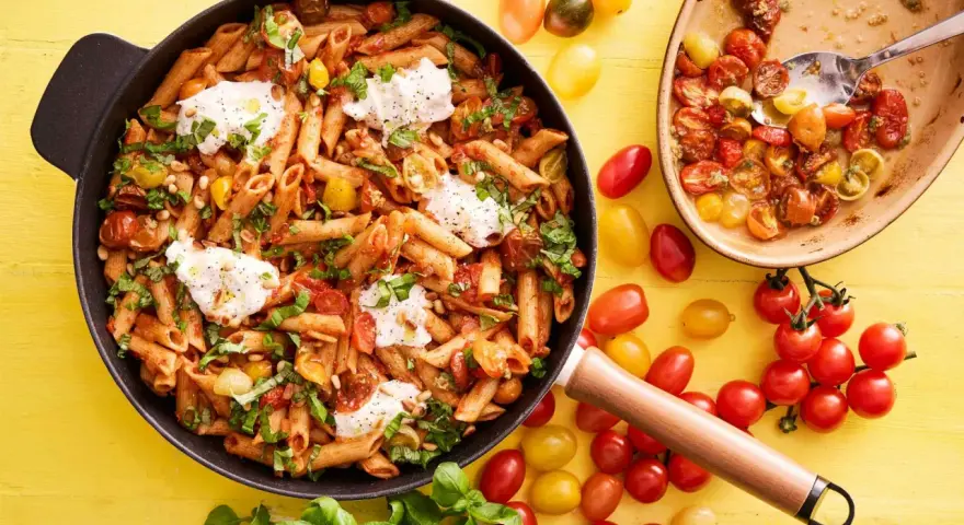 En panna med penne, körsbärstomater, basilika och mozzarella. En härlig vegetarisk mat som ser utsökt ut.