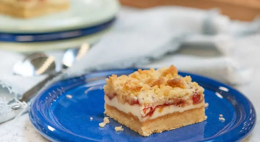 A slice of rhubarb cheesecake with a crumb topping on a blue plate.