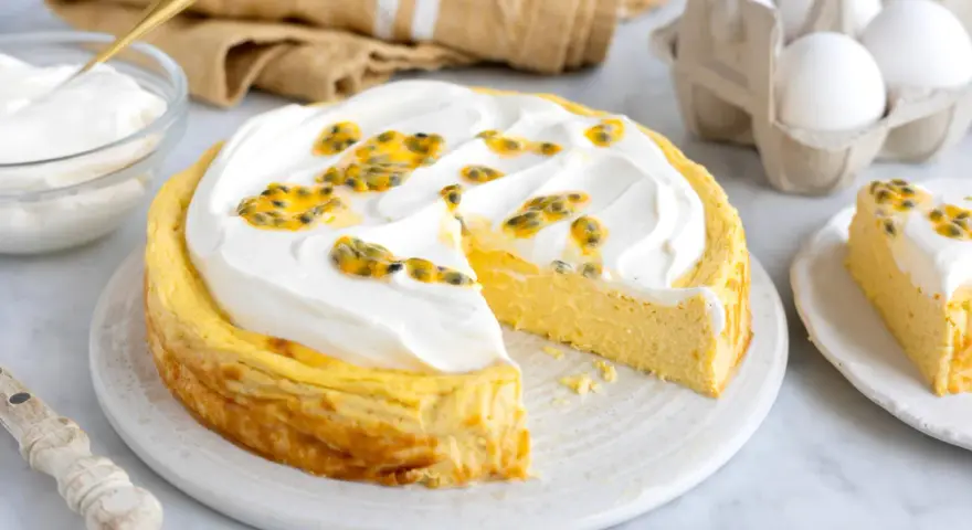 En krämig mango cheesecake med fluffig topping och passionsfrukt. En bit är redan uppskuren.