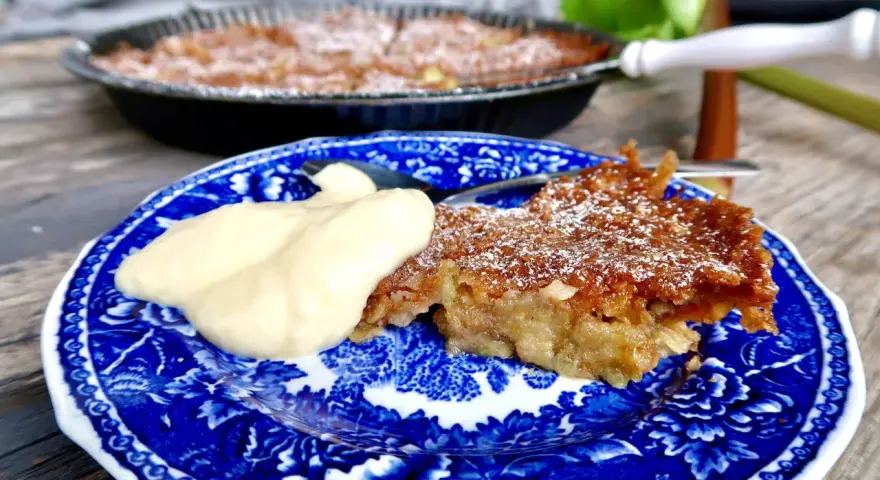 A slice of rhubarb pie with a dollop of cream on a blue and white patterned plate.