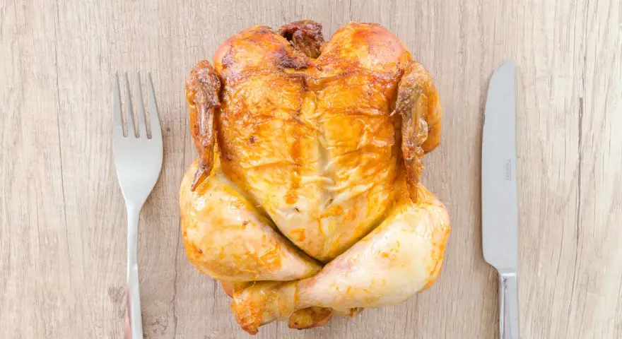 Helstekt kyckling med gaffel och kniv. En perfekt storlek för att avgöra hur mycket kyckling per person som behövs för en festmåltid.