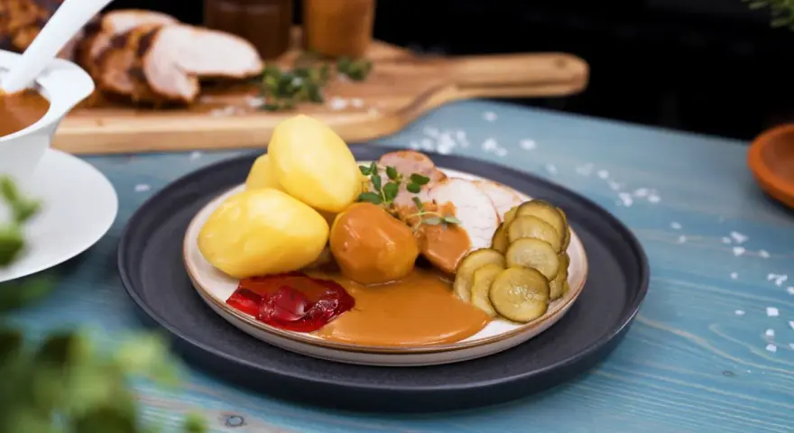 En tallrik med skivad ytterfile i sockerkaksform, potatis, sås, gelé och gurka.