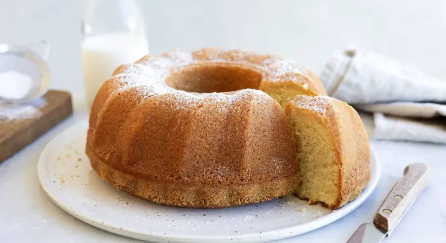 A golden-brown bundt cake dusted with powdered sugar, with a slice removed.