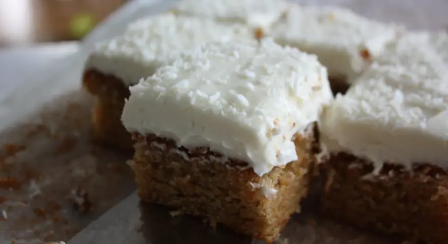 Färska bitar av morotskaka med krämig frosting och kokosflingor. En bit är uppskuren med en kniv.