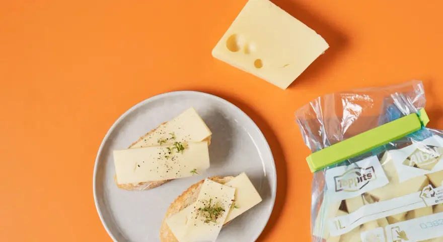 Slices of cheese on bread on a plate, a wedge of cheese, and a bag of cheese chunks.