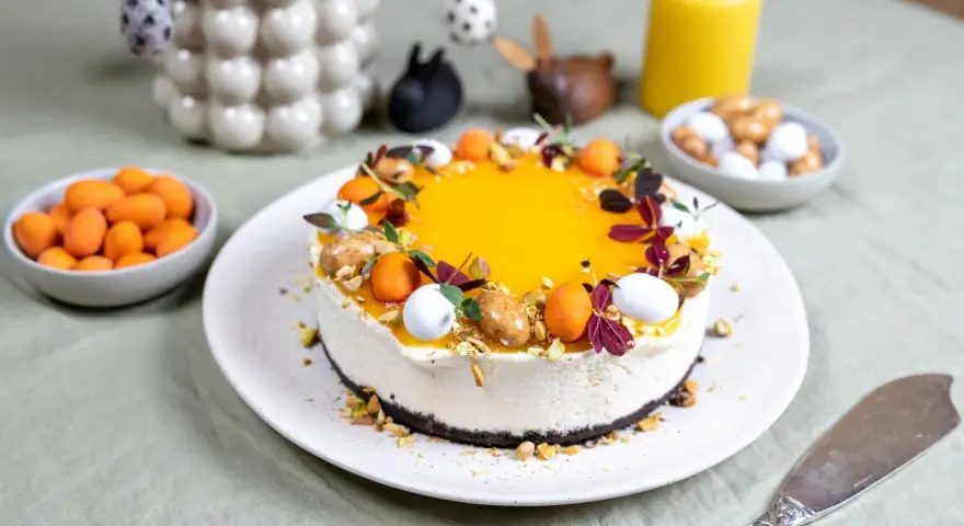 En vacker cheesecake påsk med gul topping, dekorerad med påskägg och nötter. Perfekt för påskfirandet!
