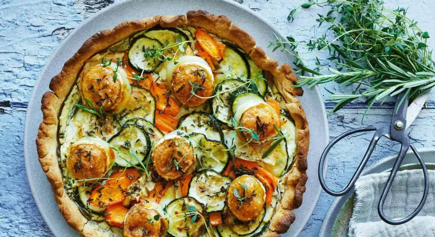 En gyllene, smakrik vegetarisk paj fylld med zucchini, morötter och toppad med ost. Garnerad med färska örter.