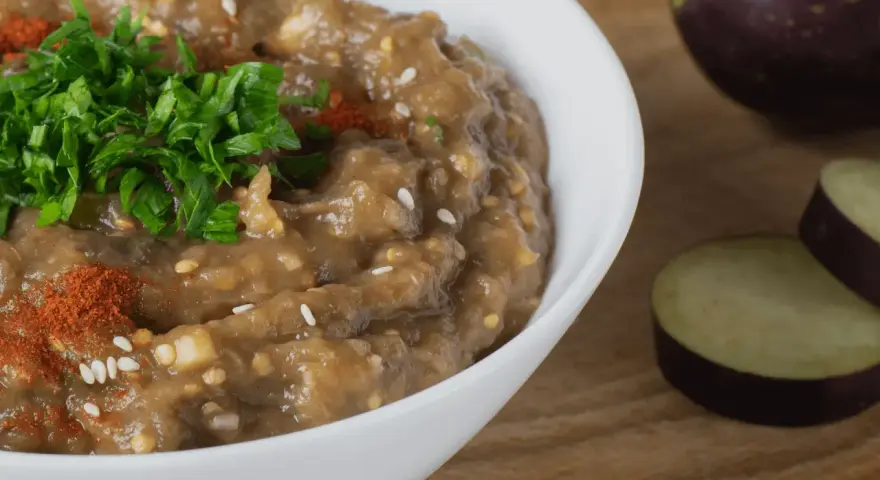 En krämig baba ganoush, toppad med färsk persilja och paprikapulver, bredvid skivade auberginer.