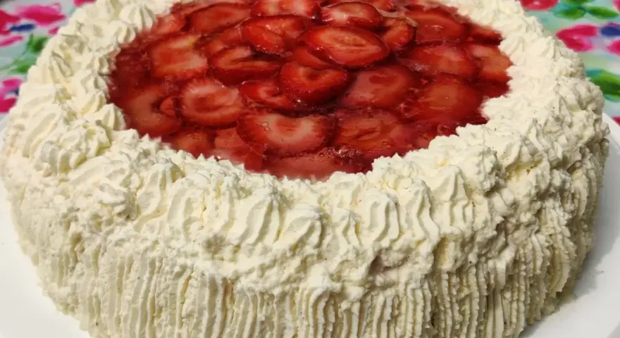A round cake with whipped cream frosting and sliced strawberries on top.