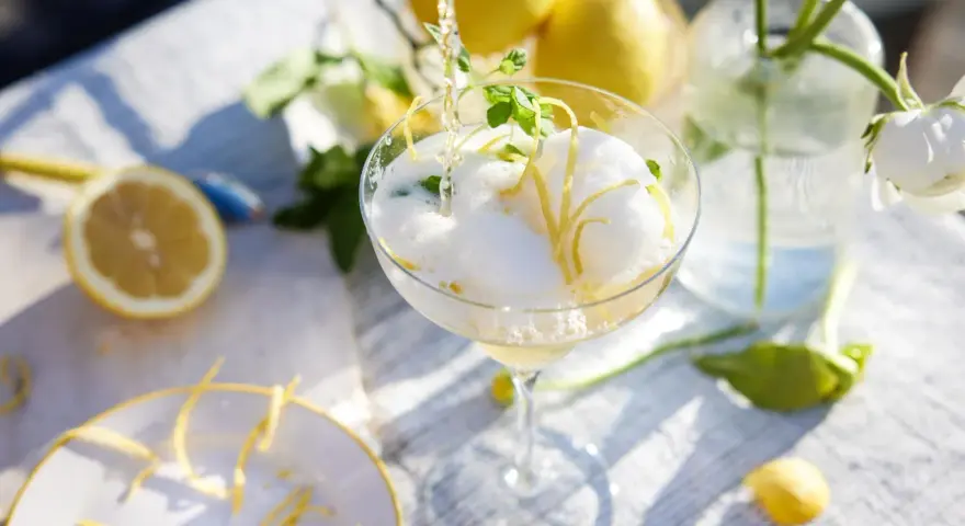 En bubblig drink med citronskal och mynta hälls upp i ett glas. Perfekt att bjuda på fika till många.