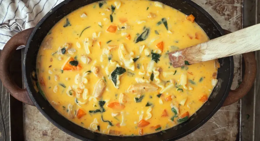 Varm och krämig kycklingsoppa med pasta, morötter och spenat i en gjutjärnspanna.