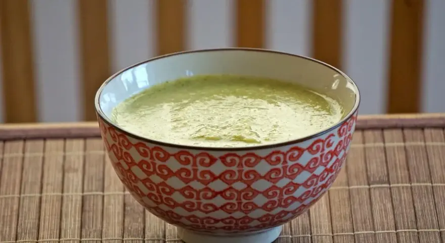 En skål med krämig blomkål och broccolisoppa, serverad på en bambumatta.