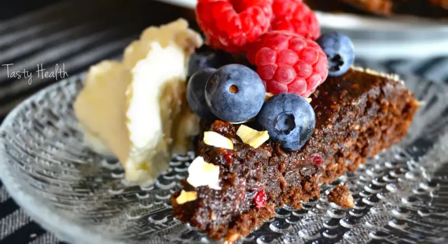 En bit nyttig kladdkaka med bär och grädde på ett mönstrat fat.