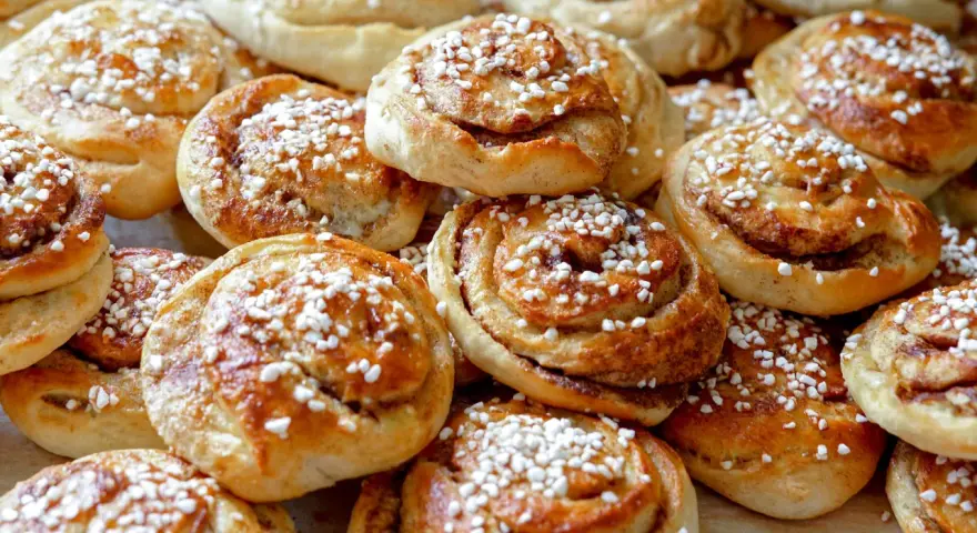 En hög med nybakade kanelbullar, strösslade med pärlsocker. Kanske bakade av Camilla Hamid för en fika.