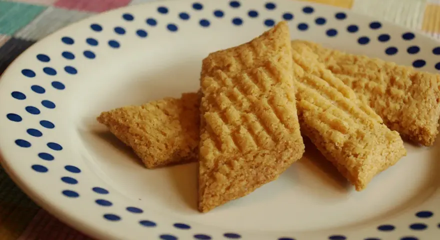 Tre gyllene glutenfria kolakakor ligger på en vit tallrik med blå prickar. De har ett rutmönster på ovansidan.