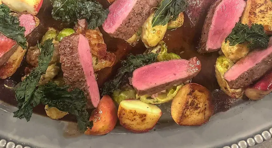 Vildsvinskött med perfekt rosa temperatur, serverat med rostade potatisar, brysselkål och grönkål i en mustig sås.