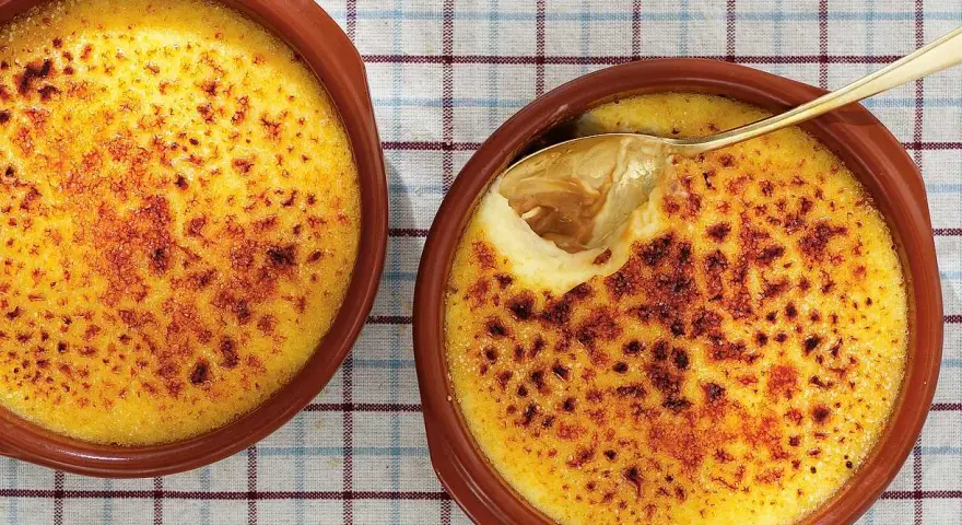 Två krämiga creme brulee i bruna skålar, en med en gyllene sked som lyfter fram den karamelliserade ytan.