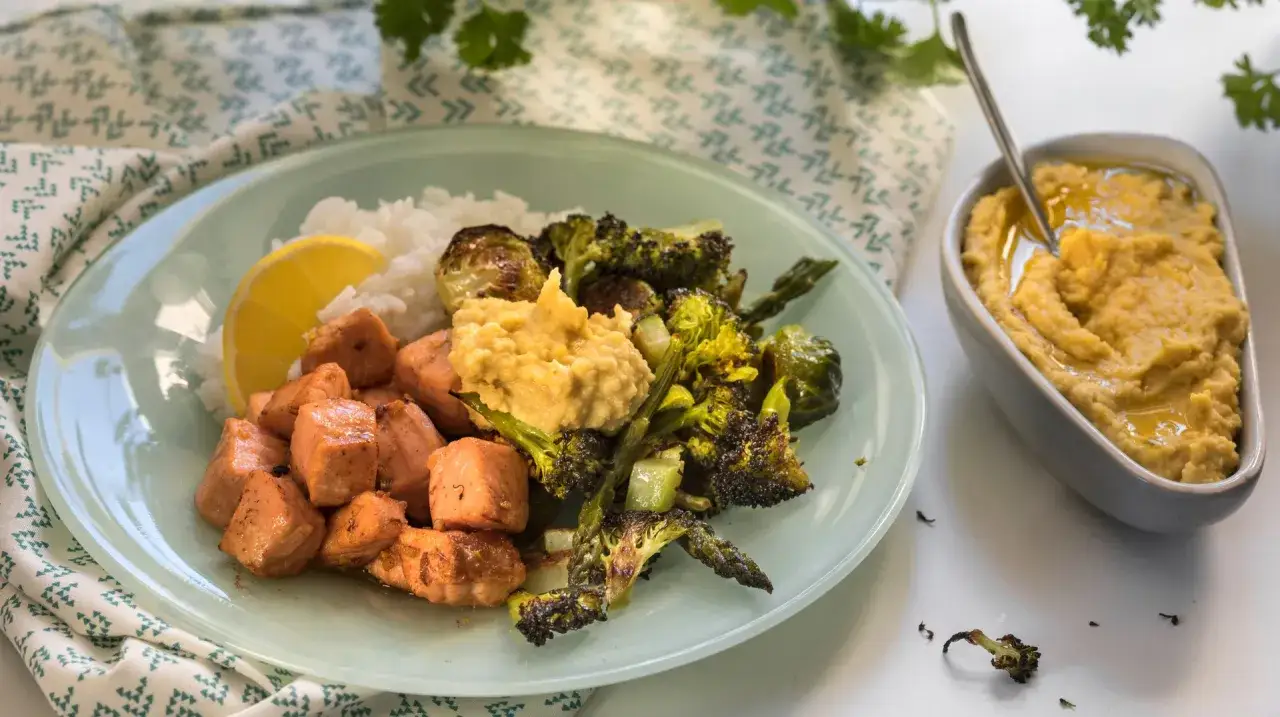 En tallrik med nyttig mat för att gå ner i vikt: laxbitar, ris, ugnsrostad broccoli och brysselkål, samt en skål hummus.