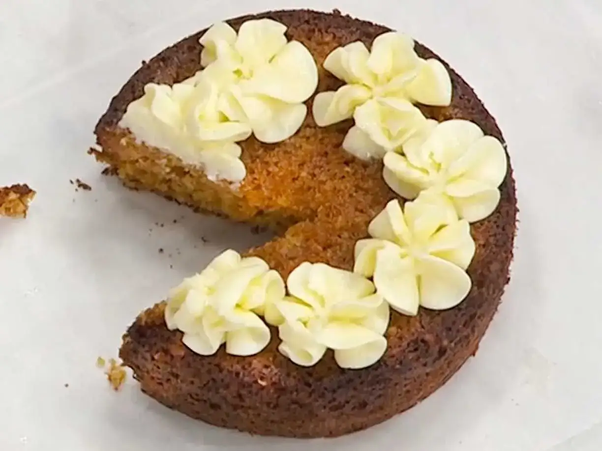 En saftig morotskaka med krämig frosting dekorerad som blommor. En bit är bortskuren.