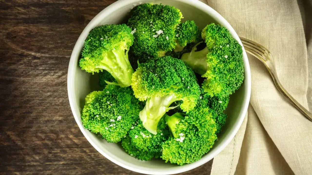 En skål med nykokt, grön broccoli, strödd med flingsalt. En gaffel ligger bredvid på en ljus duk.