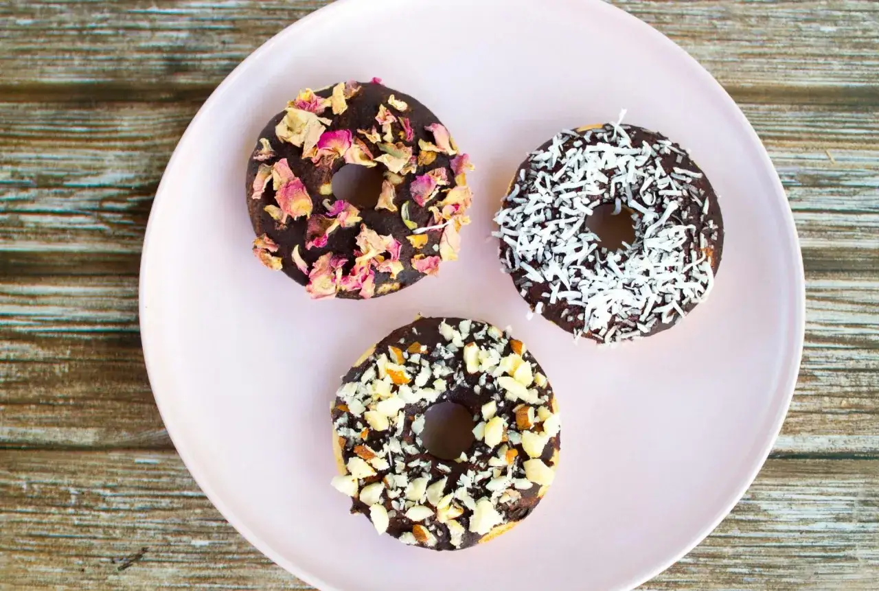 Tre chokladglaserade donuts med olika toppingar: torkade rosenblad, kokosflingor och hackade nötter. Perfekt för att baka med barn!