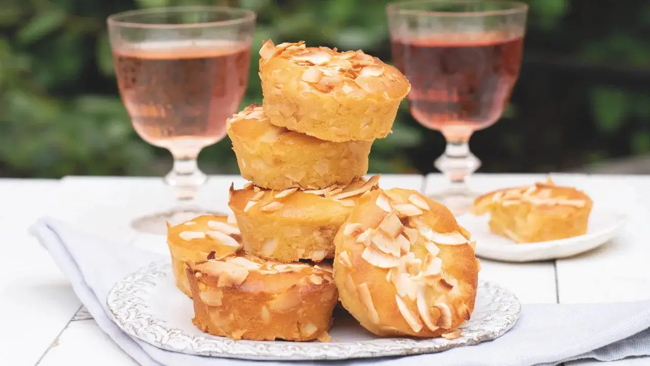 Små, gyllene muffins med mandelflagor, perfekta att baka med citron. Två glas rosé i bakgrunden.