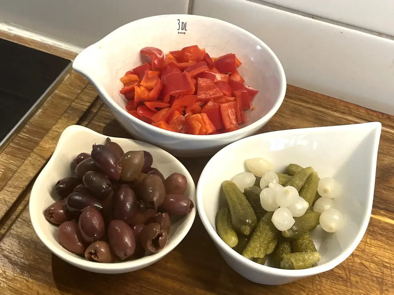 Förberedelser för en smakrik kreolsk gryta: skivad röd paprika, oliver och cornichoner med små lökar.
