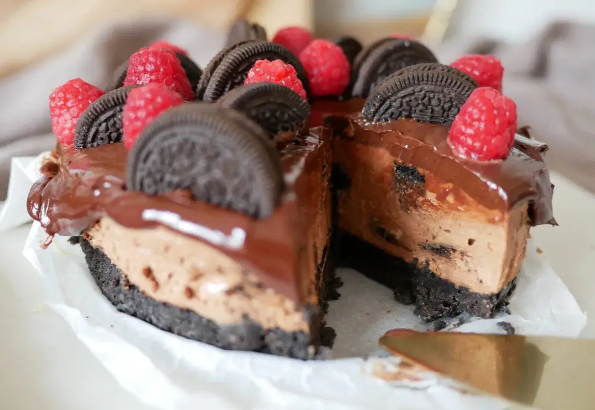 En krämig oreo cheesecake med chokladglasyr, toppad med färska hallon och oreokex. En dröm för alla chokladälskare!